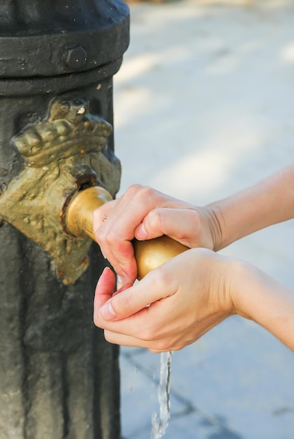 女の子は通りの古い中世の蛇口で手を洗っています 暑い街の観光客