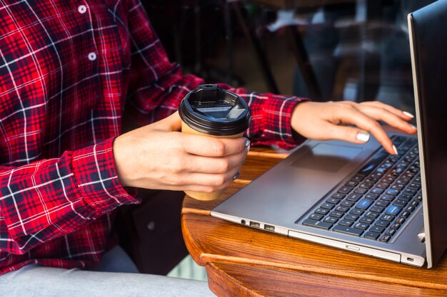 The girl is working behind a laptop at a table in a cafe next to a cup of coffee