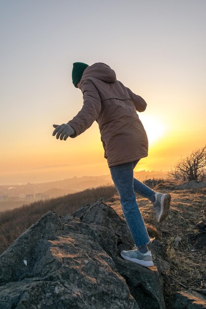 일몰 동안 산에 재킷과 모자를 쓴 소녀