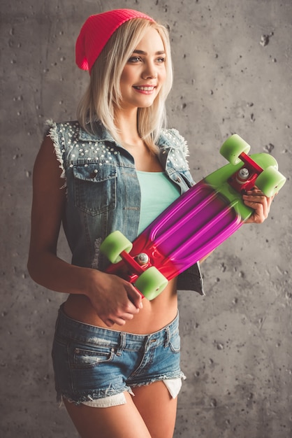 Girl in jean clothes is holding a skateboard and smiling