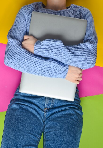 A girl in jeans and a sweater lies and hugs a laptop. Top view.