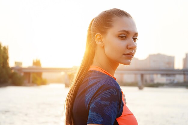 Girl jogging on the river bank looking away at sunset