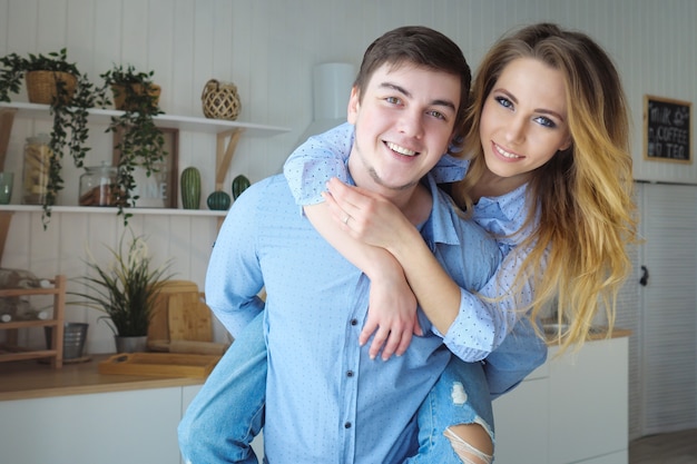 Girl jumped on guy shoulders from back laughing starts kissing man holds woman in arms against kitchen close view