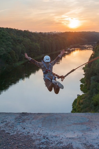 Girl jumping from the bridge. A girl with an incredible time is engaged in freestyle in bungee jumping. A young girl performs a reverse trick in bungee jumping. Jump at sunset Extreme young.