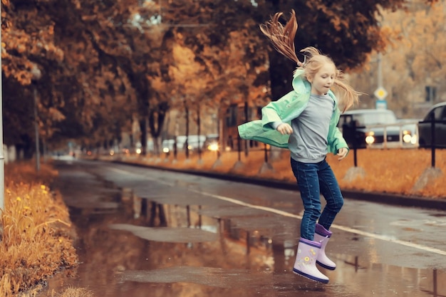 秋の雨の中、水たまりでジャンプする女の子