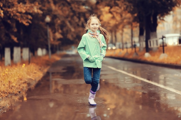 秋の雨の中、水たまりでジャンプする女の子