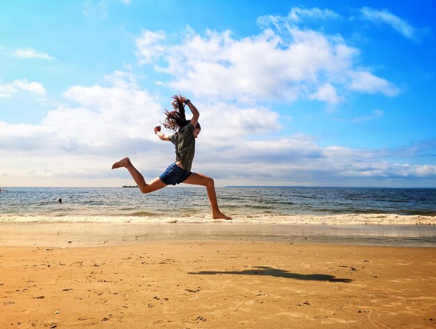 Foto ragazza che salta sulla riva della spiaggia contro il cielo