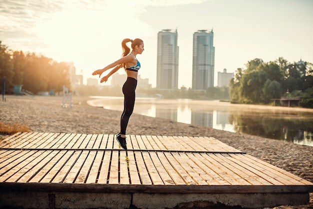 Photo girl jumping on wooden platform on river coast