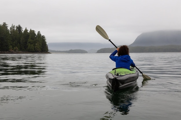 Girl kayaking in the ocean during a cloudy and gloomy sunrise