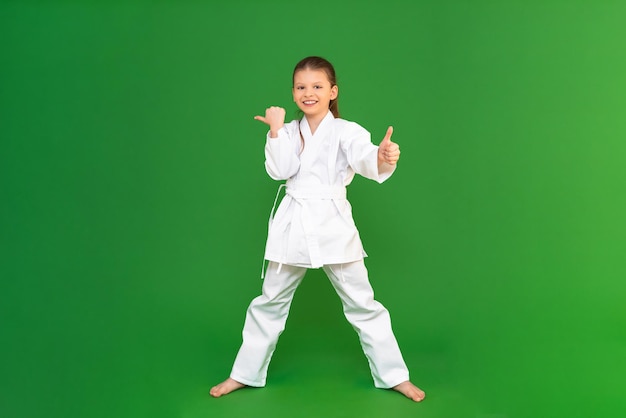 A girl in a kimono on a green background points her fingers at the advertisement kid studies martial arts child development in sports