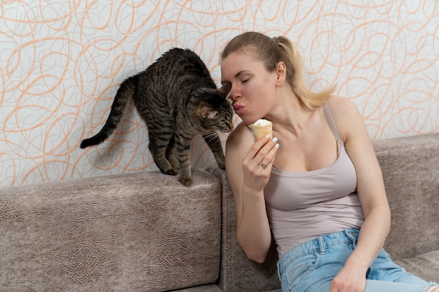 A girl kisses a cat who licks her lips while looking at ice cream in a waffle cup in the hands of the hostess