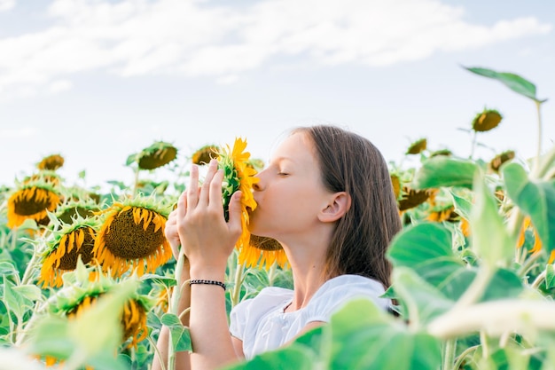 太陽の下で畑でヒマワリにキスをする女の子 栽培と収穫