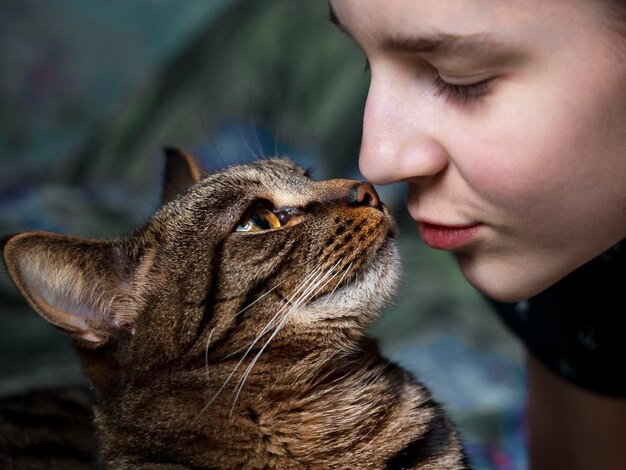 A girl kissing a cat with a blue shirt on.