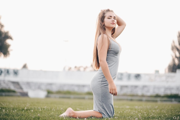 The girl kneels straightening her hair on the grass a healthy lifestyle Girl in gray fitted dress