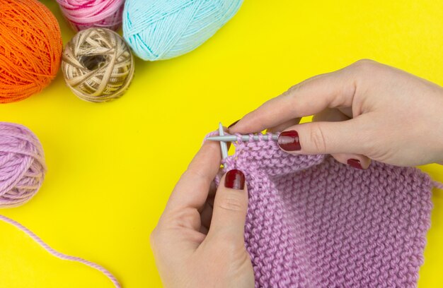 The girl knits a children's scarf on a yellow background