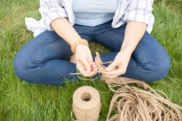 Girl knits a crochet basket on the grass, sitting in the garden on the grass. Hobby at home.