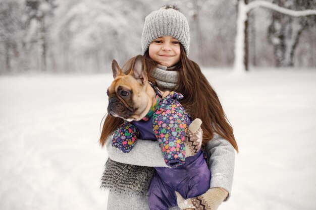 Girl in knitted hat playing with her dog french bulldog on a snow