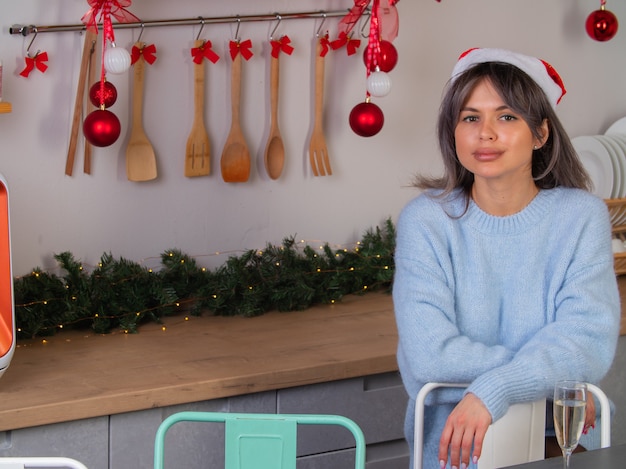 A girl in a knitted sweater and Santa hat and a glass of champagne is waiting for the start of the new year