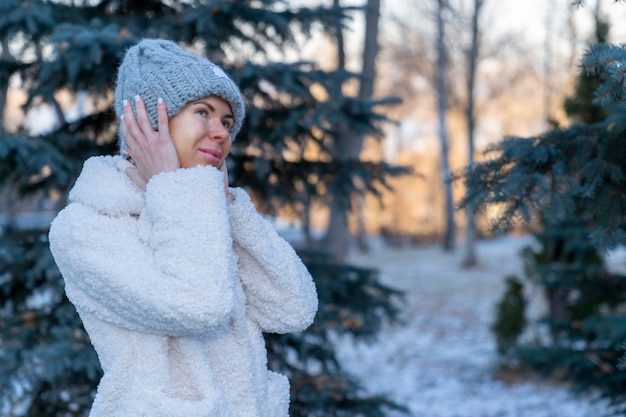 Foto una ragazza con un cappello di lana lavorato a maglia e una pelliccia di pelliccia artificiale cammina attraverso il parco invernale tra gli alberi