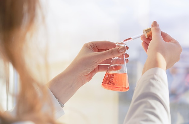 Foto una ragazza assistente di laboratorio mescola i reagenti in laboratorio in piedi vicino alla finestra