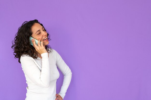 Girl laughing while talking on the phone. purple background and copy space. white casual shirt. curly hair