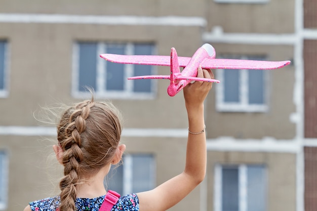 Ragazza che lancia in aria un aeroplano giocattolo rosa sullo sfondo di un edificio a più piani