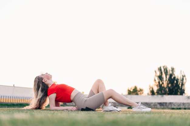 The girl lay down to rest on the lawn in a red top after training on the rope