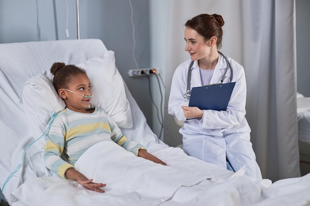 Girl laying in bed in hospital room recovery and talking to nurse