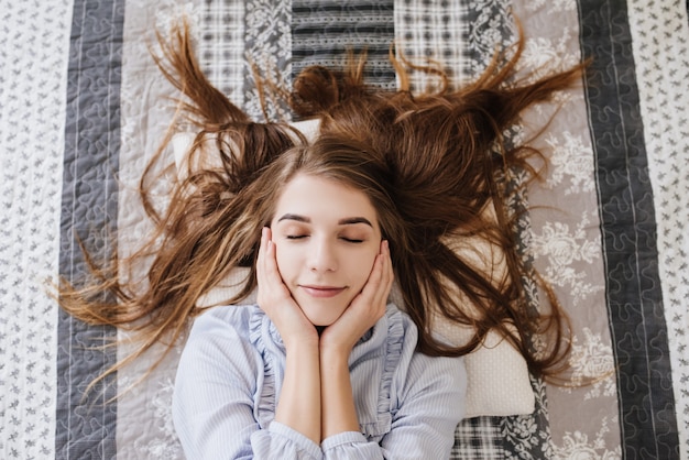 The girl laying in her pajamas on the bed in her room. Stylish gray-white interior.