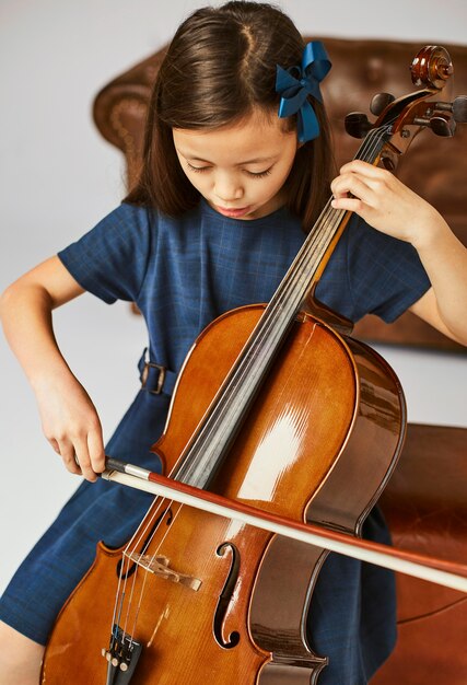 家でチェロを弾く方法を学ぶ女の子