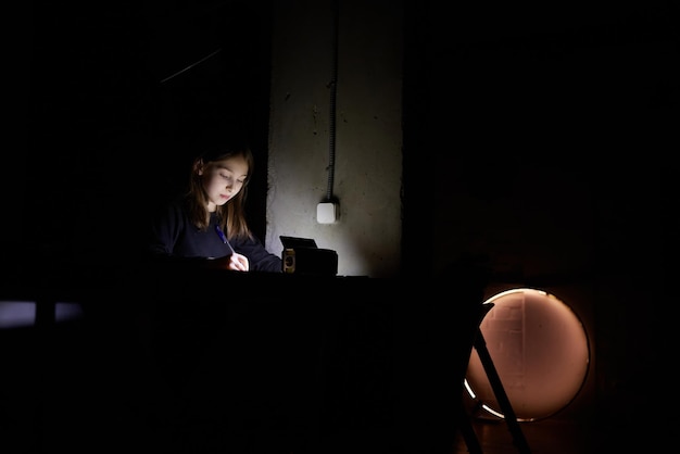 The girl learns lessons in the dark a child does school work\
when there is no electricity at home