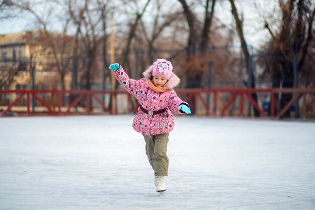 女の子は冬の路上でアイススケートリンクでスケートをすることを学ぶ