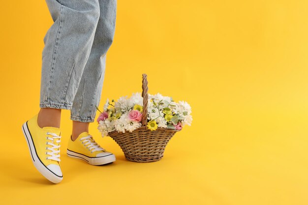 Girl legs and basket of flowers on yellow background