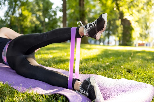 Girl legs with rubber elastic band during workout outdoors young womane exercising with additional e