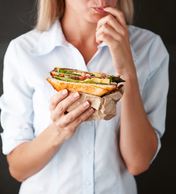 Девушка облизывает пальцы, держа вкусный бутерброд