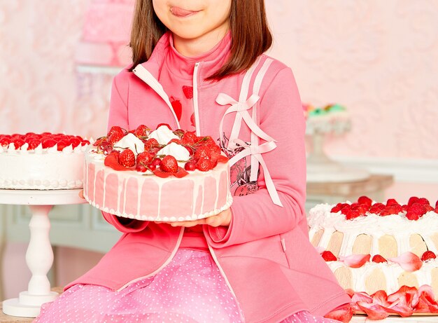 The girl licks her lips on a strawberry cake.
