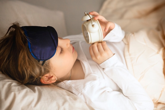 Foto la ragazza si trova a letto la mattina e guarda la sveglia.