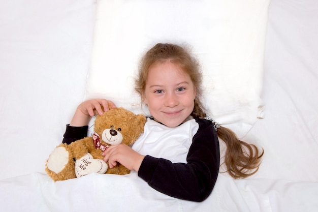 Girl lies in bed with a bear and smiles