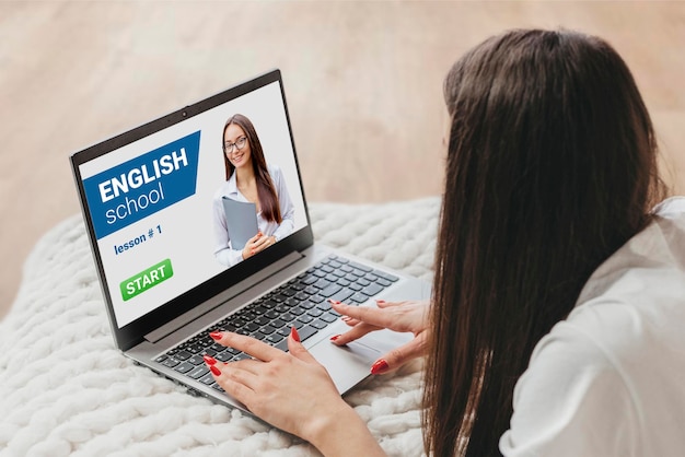 A girl lies on a bed with a laptop and studies online English lessons