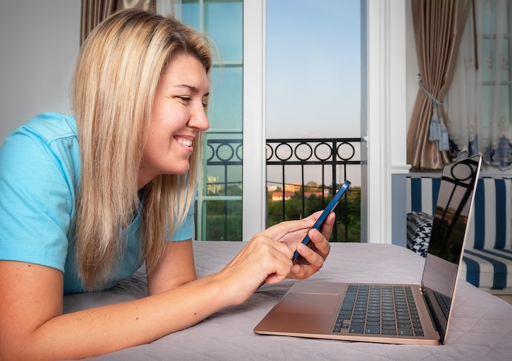 Photo a girl lies on the bed working with a laptop and phone