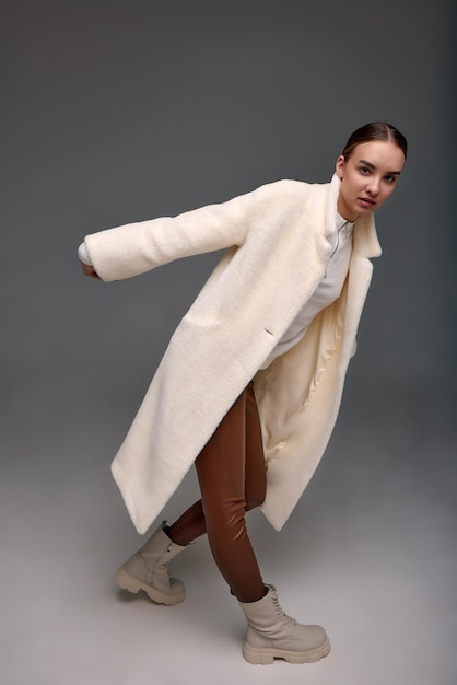 A girl in a light artificial fur coat on a gray background modern fashion trend for fur coats made o