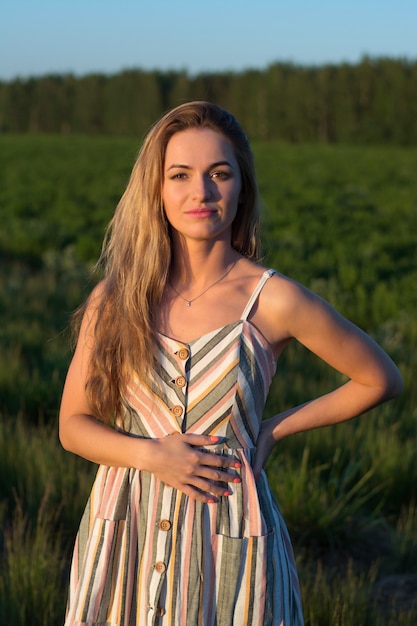 A girl in a light dress in a green field at sunset