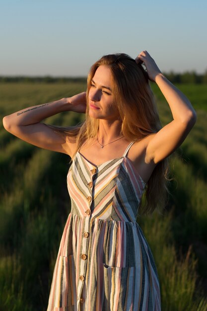 A girl in a light dress in a green field at sunset