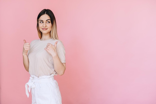 A girl in a light Tshirt shows a thumbs up with both hands on a pink background