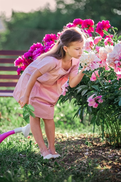 Ragazza in un abito di lino che si prende cura delle peonie in estate in giardino