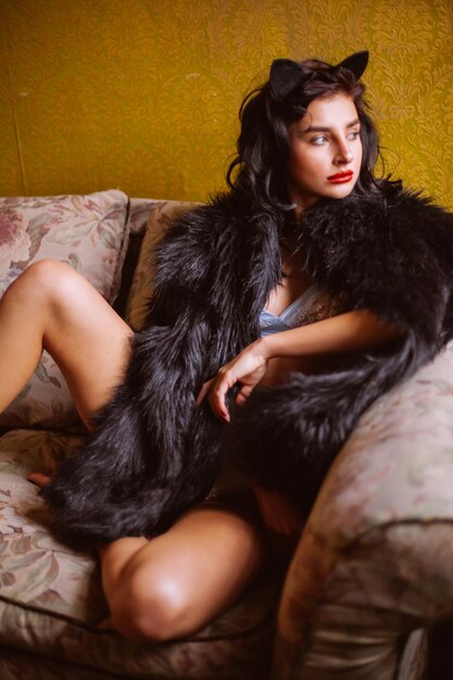 Girl in lingerie and a black coat with curly black hair posing in vintage interior vintage photo