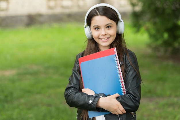 オーディオを聞いている女の子は、学校の学校のクラブの概念に向かう途中で教科書を運ぶ