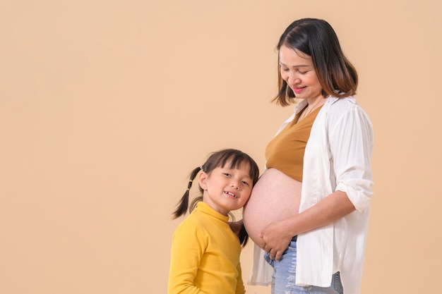 Girl listening baby's heartbeat hugging pregnant mother's belly