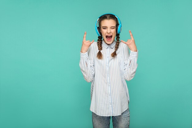 Girl listening favorite music with headphone looking at camera with surprised face and rock sign