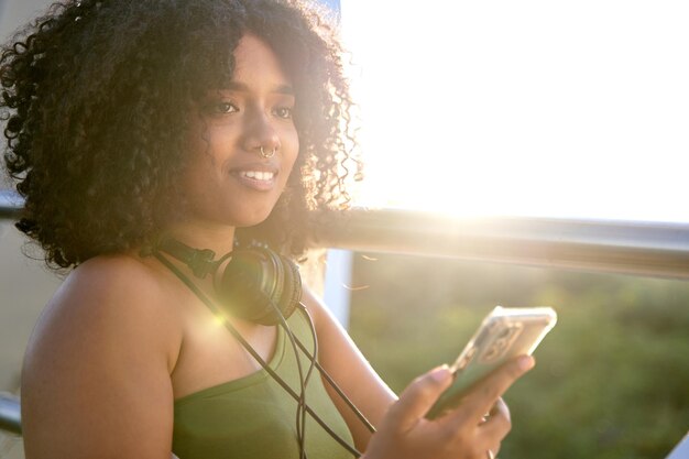 彼女の携帯電話から音楽を聴いている女の子巻き毛とヘッドフォンを屋外で持つ若い女性